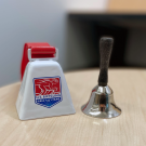 A red and white cowbell next to a silver handbell